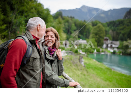 Active elderly couple hiking together in autumn mountains. Senior tourists enjoying view on lake 113354500