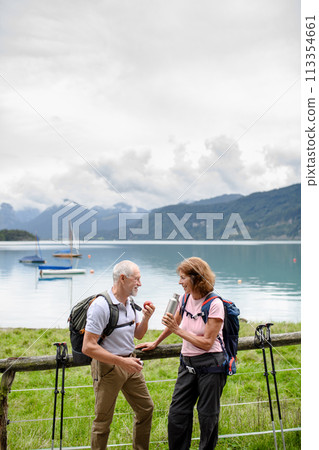Active elderly couple hiking together in mountains. Drinking coffee and having healthy snack, to get energy. Senior tourist with backpacks resting during hike. 113354661