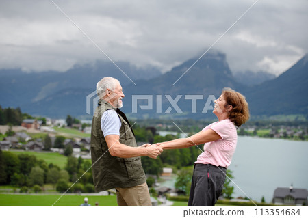 Active elderly couple on trip together, during spring day. Senior tourists visiting, exploring new places. Side view, holding hands. 113354684