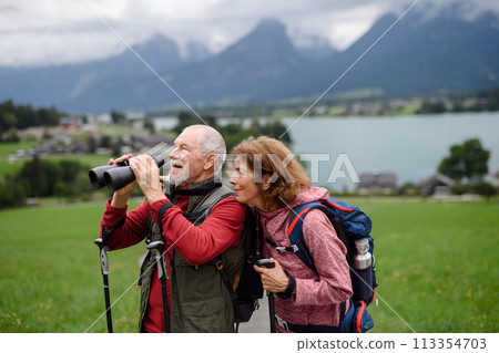 Active elderly couple hiking together in autumn mountains. Senior tourists enjoying nature look through binoculars. Active elderly couple hiking together in autumn mountains. Senior tourists enjoying nature look through binoculars. 113354703