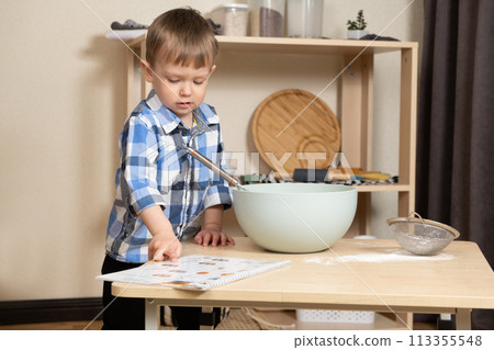 Little boy making pastries according to the recipe book for toddlers. Little boy making pastries according to the recipe book for toddlers. 113355548