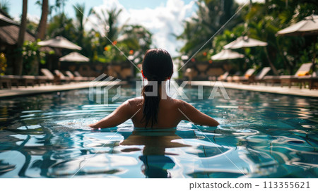 Beautiful woman on vacation relaxing in swimming pool at luxury tropical resort. Back view 113355621