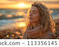 Beautiful young woman enjoys sunset on beach, with eyes closed, warm 113356145