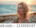 Beautiful serene young woman enjoys sunrise on beach, with soft focus 113356147
