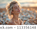 Serene young woman in romantic attire enjoys sunrise on pebble beach 113356148