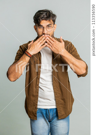 Frightened Indian man closing mouth with hands refusing to tell terrible secret, unbelievable truth 113356590