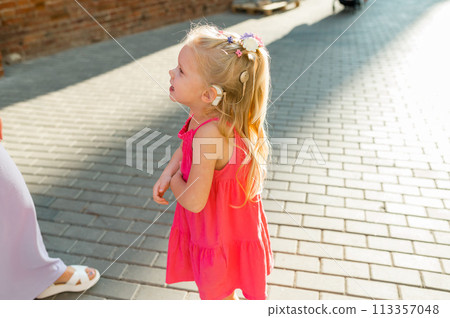 Child girl with hearing aid cochlear implant in pink dress having fun on summer street. Aid for the treatment of deafness and hearing loss in humans. Copy space Child girl with hearing aid cochlear implant in pink dress having fun on summer street. Aid for the treatment of deafness and hearing loss in humans. Copy space 113357048