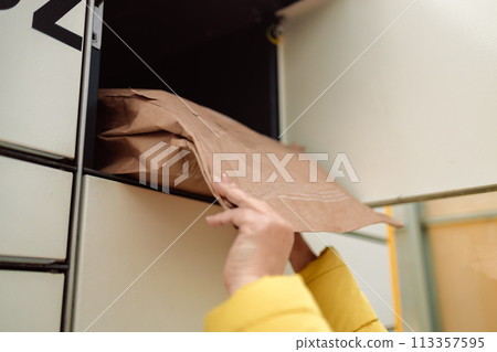Woman with box at outdoor automated parcel machine. Modern parcel locker with many postal boxes outdoors Woman with box at outdoor automated parcel machine. Modern parcel locker with many postal boxes outdoors 113357595
