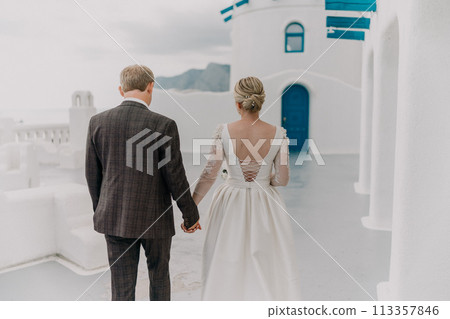 A bride and groom are walking down a path in front of a blue door. The bride is wearing a white dress and the groom is wearing a suit. Scene is romantic and happy. A bride and groom are walking down a path in front of a blue door. The bride is wearing a white dress and the groom is wearing a suit. Scene is romantic and happy. 113357846