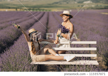 woman child sitting bench in field lavender. The woman is holding a bouquet of flowers, and the child is holding a bouquet as well. The scene is peaceful and serene. 113357871