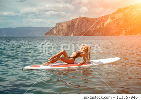 Woman sup sea. Sports girl on a surfboard in the sea on a sunny summer day. In a black bathing suit, he sits on a sapa in the sea. Rest on the sea. Woman sup sea. Sports girl on a surfboard in the sea on a sunny summer day. In a black bathing suit, he sits on a sapa in the sea. Rest on the sea. 113357940