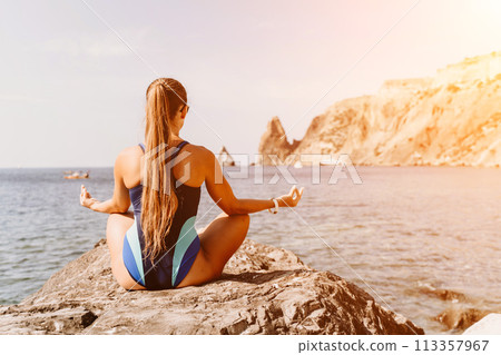 Yoga on the beach. A happy woman meditating in a yoga pose on the beach, surrounded by the ocean and rock mountains, promoting a healthy lifestyle outdoors in nature, and inspiring fitness concept. 113357967