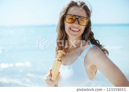 smiling modern female on ocean coast with sunscreen 113358051