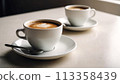 A hot cup of coffee on a saucer, set against a white background, casting a subtle shadow. 113358439