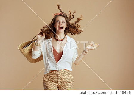 smiling woman in blouse and shorts jumping on beige 113358496