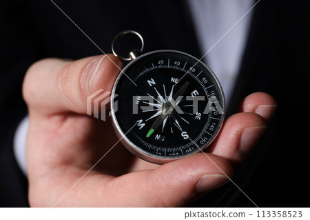 A compass, in the hands of a man, on a dark background. 113358523