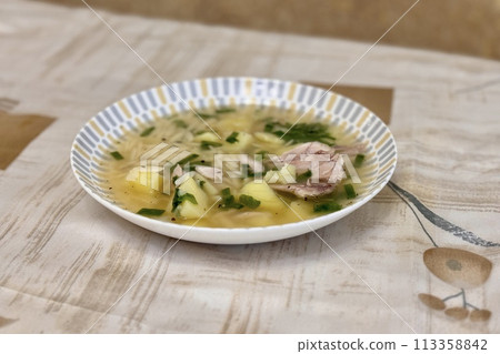 Bowl of traditional chicken soup served in a white plate on background tablecloth. Close-up 113358842