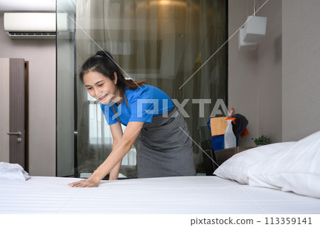 Female housekeeper changing clean bedsheets in hotel room Female housekeeper changing clean bedsheets in hotel room 113359141