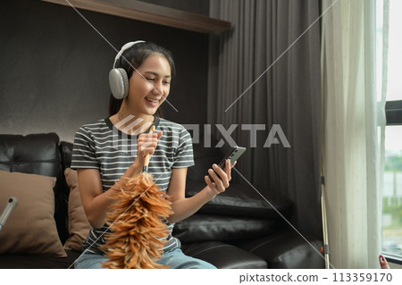 Happy woman listening to music and using mobile phone after finished housework Happy woman listening to music and using mobile phone after finished housework 113359170