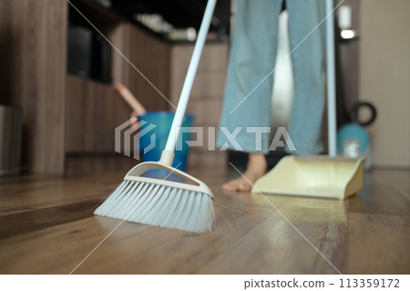 Young woman doing chores in kitchen sweeping floor with broom Young woman doing chores in kitchen sweeping floor with broom 113359172