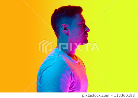 Side view portrait of young handsome man posing in white T-shirt in neon light against vibrant yellow studio background. 113360198