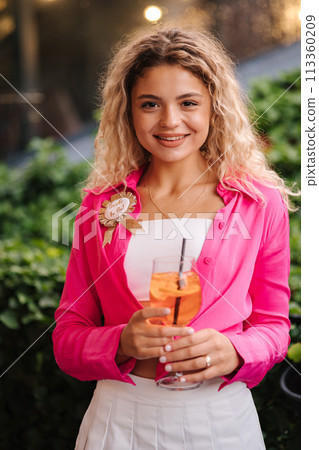 Beautiful young woman hold alcoholic cocktail in hands. Bride to be. Woman with curly hair drink aperol spritz  113360209