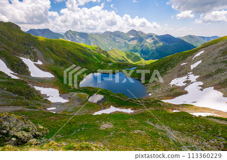 alpine landscape of fagaras mountains. capra lake of romania in summer. sunny weather with clouds on the blue sky. spots of snow and grass on the rocky hillside. stunning travel destination 113360229