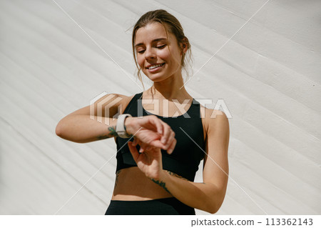 Smiling woman in sportswear looking on smartwatch after training. Outdoor sports in the morning Smiling woman in sportswear looking on smartwatch after training. Outdoor sports in the morning 113362143