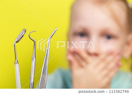 Dental instruments against the background of a frightened girl who covers her mouth with her hands. The concept of children being afraid of dentists. Dentophobia. Psychological attitude towards 113362748