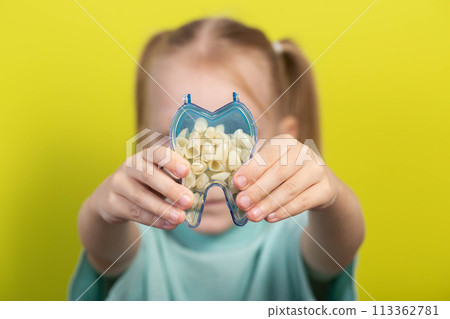A model of an artificial tooth in the hands of a little girl of seven years old on a yellow background. The concept of correcting malocclusion and uneven teeth in children. Children's orthodontics 113362781
