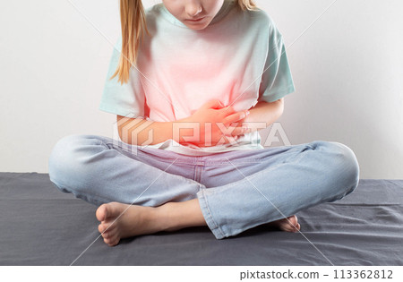 A little girl sits and holds her sore red stomach with her hands. Cognition of liver and gallbladder diseases in children. Cholelithiasis, biliary dyskinesia, cholecystitis A little girl sits and holds her sore red stomach with her hands. Cognition of liver and gallbladder diseases in children. Cholelithiasis, biliary dyskinesia, cholecystitis 113362812
