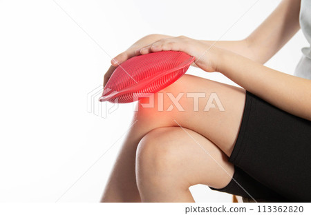 A little girl applies a red heating pad with hot water to her knee joint. Relieving pain with heat. Sprains in children, close-up. Copy space for text A little girl applies a red heating pad with hot water to her knee joint. Relieving pain with heat. Sprains in children, close-up. Copy space for text 113362820