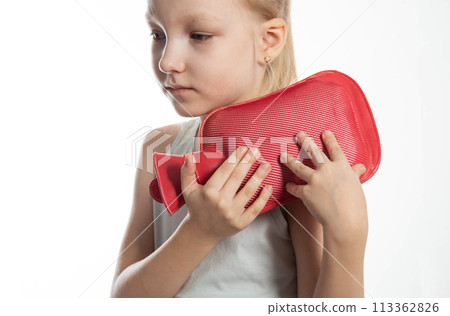 A little girl applies a heating pad with warm water to her shoulder joint for a sprained ligament. Heat treatment, close-up 113362826