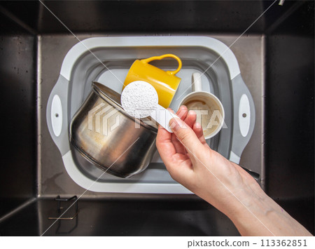 a measuring spoon with granules of environmentally friendly oxygen bleach is in the girl s hand. A modern means for cleaning and washing dirty dishes, close-up a measuring spoon with granules of environmentally friendly oxygen bleach is in the girl s hand. A modern means for cleaning and washing dirty dishes, close-up 113362851