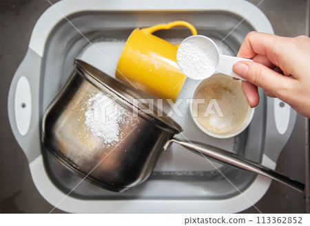 a measuring spoon with granules of environmentally friendly oxygen bleach is in the girl s hand. A modern means for cleaning and washing dirty dishes, close-up 113362852