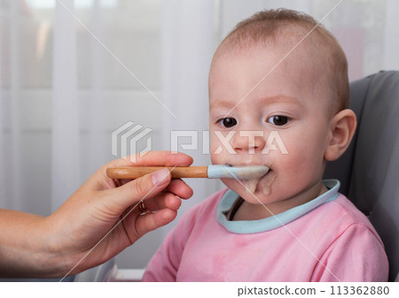 A mother's hand with a spoon and buckwheat porridge feeds a baby boy aged one year. Nutrition of children at an early age. Baby baby health food. Copy space for text, microelements A mother's hand with a spoon and buckwheat porridge feeds a baby boy aged one year. Nutrition of children at an early age. Baby baby health food. Copy space for text, microelements 113362880