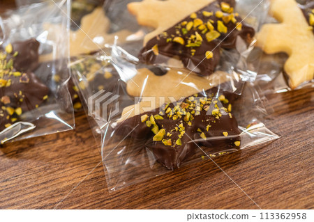 Carefully packaging Christmas cutout cookies, half-dipped in chocolate and presented in clear cellophane wrapping, perfect for festive gifting. 113362958