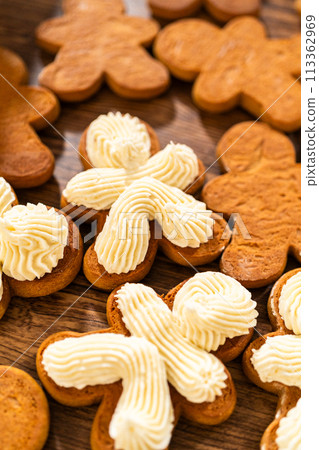 Making gingerbread man cookie sandwiches filled with eggnog buttercream, arrayed on a rustic wooden table, ideal for heartfelt Christmas gifting. Making gingerbread man cookie sandwiches filled with eggnog buttercream, arrayed on a rustic wooden table, ideal for heartfelt Christmas gifting. 113362969