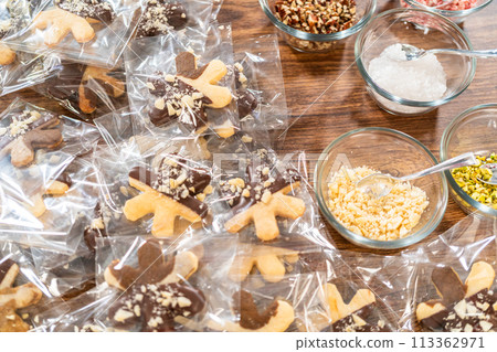 Carefully packaging Christmas cutout cookies, half-dipped in chocolate and presented in clear cellophane wrapping, perfect for festive gifting. 113362971