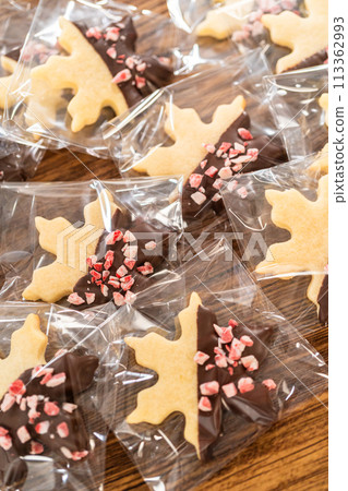 Carefully packaging Christmas cutout cookies, half-dipped in chocolate and presented in clear cellophane wrapping, perfect for festive gifting. Carefully packaging Christmas cutout cookies, half-dipped in chocolate and presented in clear cellophane wrapping, perfect for festive gifting. 113362993