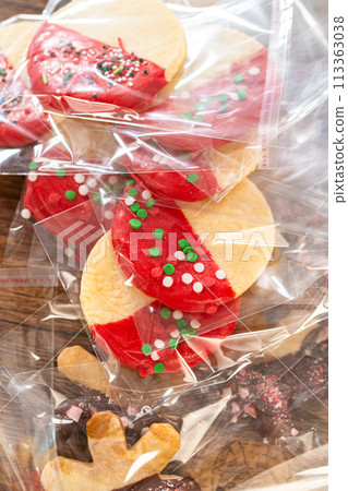 Carefully packaging Christmas cutout cookies, half-dipped in chocolate and presented in clear cellophane wrapping, perfect for festive gifting. Carefully packaging Christmas cutout cookies, half-dipped in chocolate and presented in clear cellophane wrapping, perfect for festive gifting. 113363038