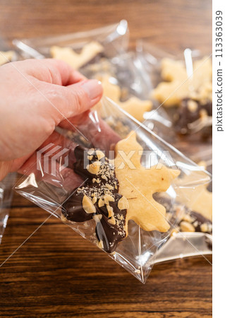 Carefully packaging Christmas cutout cookies, half-dipped in chocolate and presented in clear cellophane wrapping, perfect for festive gifting. Carefully packaging Christmas cutout cookies, half-dipped in chocolate and presented in clear cellophane wrapping, perfect for festive gifting. 113363039