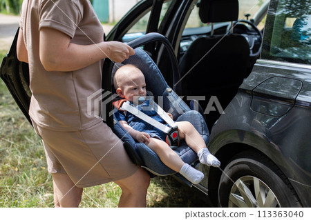 The mother puts the infant car seat with the child in the car. The concept of child safety in the car. Transportation of children 113363040