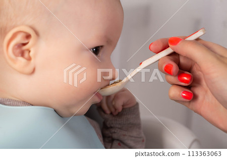 A mother feeds porridge from a spoon to a little boy who is 8 months old. Feeding infants. A mother feeds porridge from a spoon to a little boy who is 8 months old. Feeding infants. 113363063