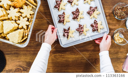 Flat lay. Carefully packaging Christmas cutout cookies, half-dipped in chocolate, sprinkled with crushed nuts, and presented in clear cellophane wrapping. 113363166