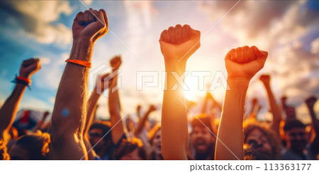 Raised fists of a crowd against a sunset sky 113363177