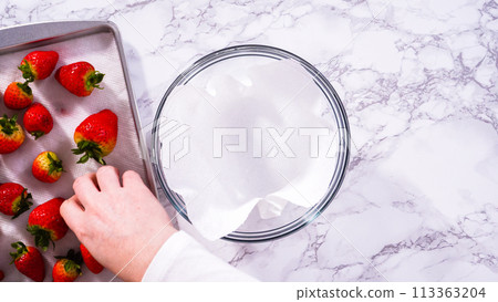 Flat lay. Strawberries, freshly washed and dried, are neatly stored in a glass bowl lined with a paper towel and securely covered with plastic wrap to maintain freshness. 113363204