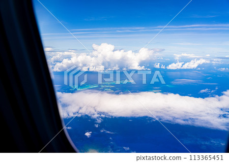 In-flight resort summer vacation travel airplane sea wing inbound window clouds island beach coral 113365451