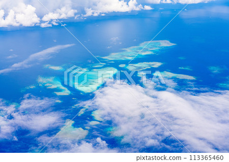 In-flight resort summer vacation travel airplane sea wing inbound window clouds island beach coral In-flight resort summer vacation travel airplane sea wing inbound window clouds island beach coral 113365460