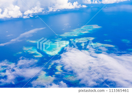 In-flight resort summer vacation travel airplane sea wing inbound window clouds island beach coral 113365461